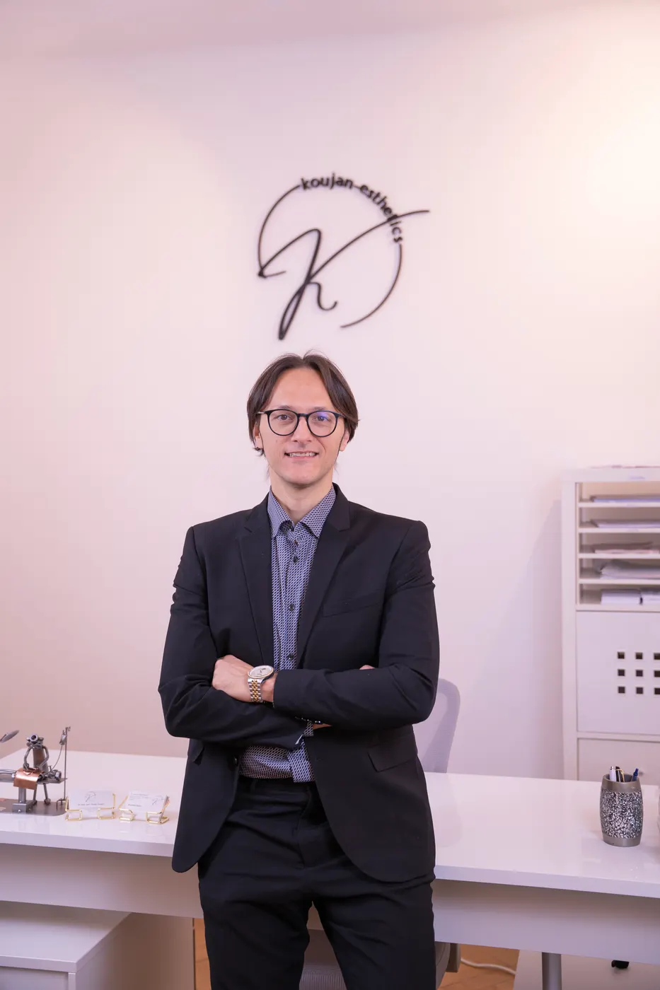 Dr. Modar Koujan im Anzug vor dem koujan-esthetics-Logo in seiner Ordination in Wien